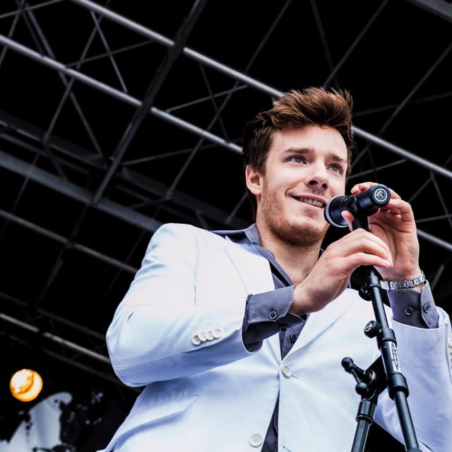 Mann på scenen med blå blazer som smiler med mikrofon 