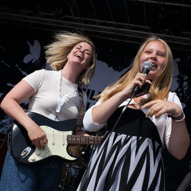 To jenter som synger på scenen, en med gitar og en med mikrofon 